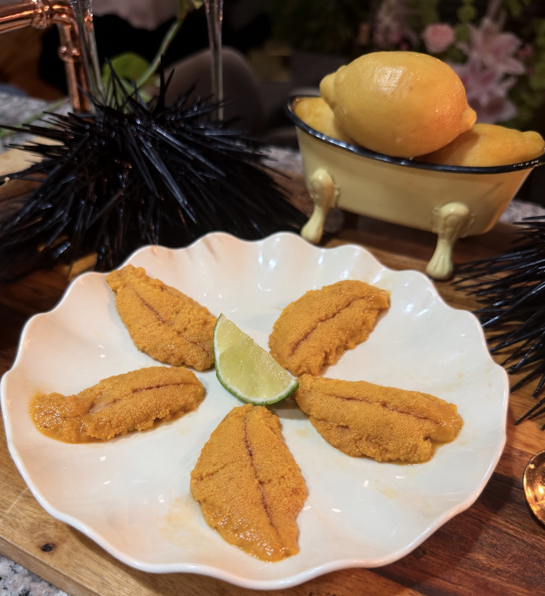 Five uni lobes from whole live California red sea urchin with a lime wedge on a white scalloped plate